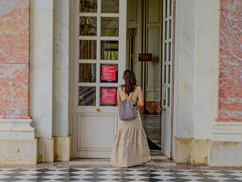 Mujer de pie frente a una puerta, con una expresión neutral y vestimenta casual.