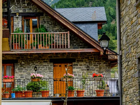 Fachada de casa de piedra tradicional en Jaca, Pirineo Aragonés, con balcones de madera decorados con macetas y flores.