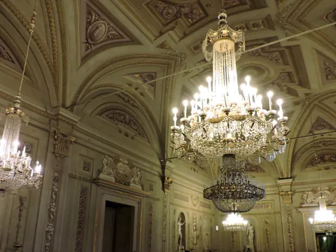 Salón elegante del Palacio Pitti en Florencia, con techos abovedados decorados, esculturas clásicas y grandes lámparas de araña de cristal iluminadas.