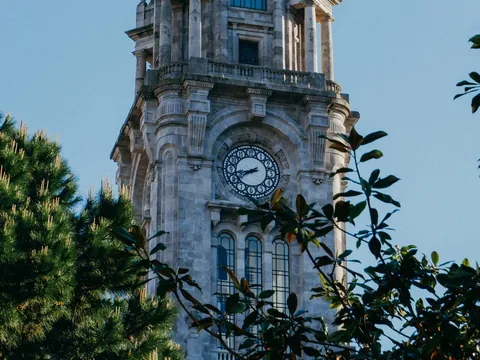 Torre con reloj en Oporto vista entre árboles en un día despejado.