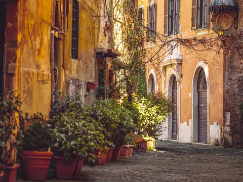 Calle tranquila de Trastevere en Roma con fachadas ocres y macetas llenas de plantas