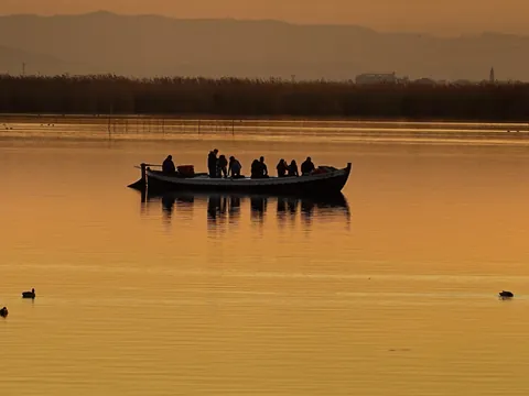 Una barca tradicional cruza el lago mientras el sol se refleja en el agua.