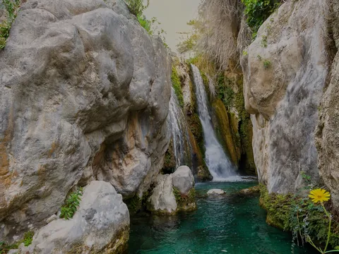 Cascada en las Fuentes del Algar rodeada de rocas, vegetación y agua clara.