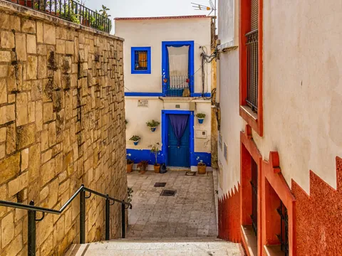 Calle estrecha con fachada blanca y detalles azules en el barrio de Santa Cruz, Alicante