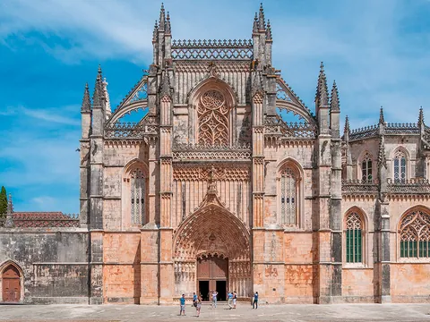 Fachada del Monasterio de Batalha con detalles góticos y visitantes en la plaza.