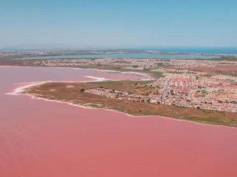 Vista aérea de la Laguna Rosa de Torrevieja con su intenso color rosa, zonas residenciales y la laguna azul de fondo.