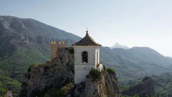 Campanario de Guadalest sobre un peñasco, rodeado de montañas y paisaje natural.