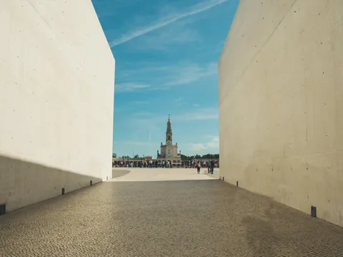 Vista del Santuario de Fátima, Portugal, enmarcada por muros de hormigón, con la torre de la Basílica de fondo.