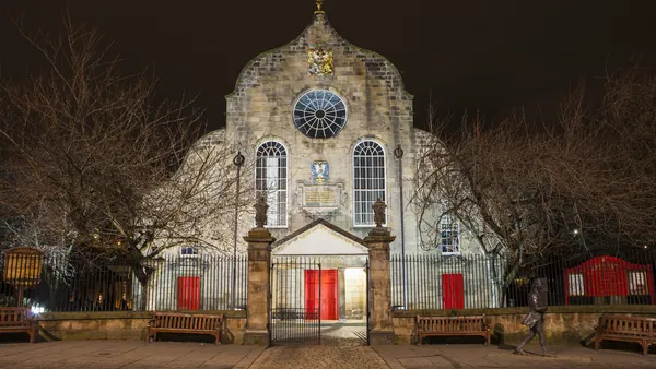 Canongate Kirk iluminada por la noche mostrando su fachada blanca con puertas rojas en Edimburgo