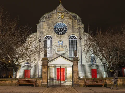Canongate Kirk iluminada por la noche mostrando su fachada blanca con puertas rojas en Edimburgo