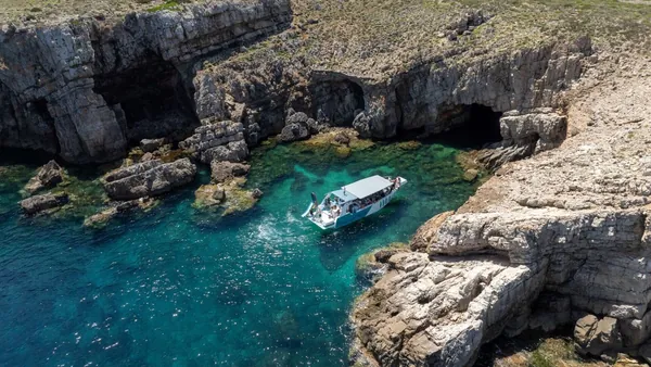Barco de excursión navegando por cuevas y acantilados del norte de Menorca