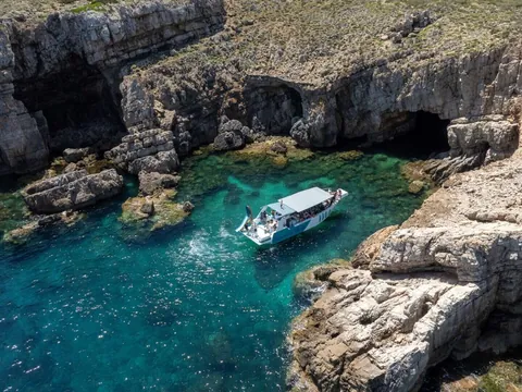 Barco de excursión navegando por cuevas y acantilados del norte de Menorca