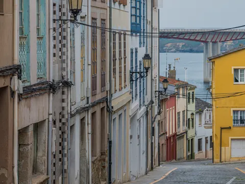 Calle del casco antiguo de Ribadeo con fachadas coloridas, vistas al mar Cantábrico y al puente de los Santos al fondo.