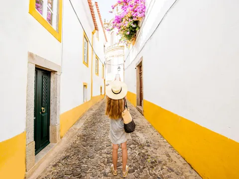 Calle blanca y amarilla de Évora, Portugal, con una turista caminando.