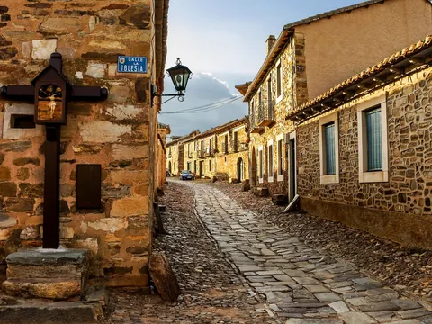 Calle empedrada tradicional en Castrillo de los Polvazares, León, con casas de piedra maragata y un crucero antiguo.