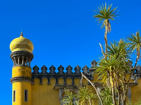 Cúpula amarilla del Palacio da Pena junto a palmeras bajo un cielo azul intenso.