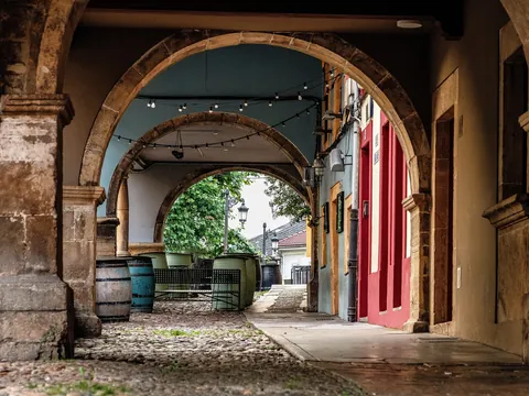 Arcos de piedra en una calle del casco antiguo de Avilés, con mesas y barriles típicos bajo los soportales asturianos.