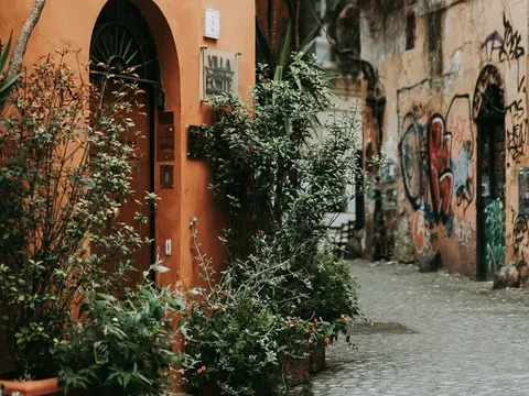 Calle con fachadas envejecidas y plantas en Trastevere, Roma, con muros grafiteados