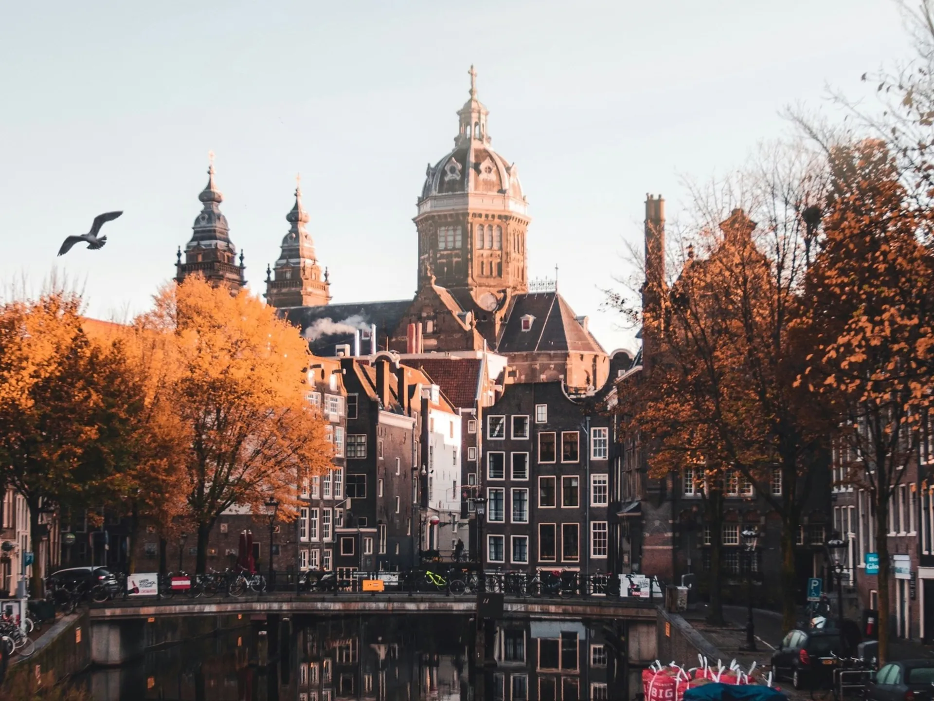 Canal de Ámsterdam con edificios clásicos, árboles de otoño y la Basílica de San Nicolás.