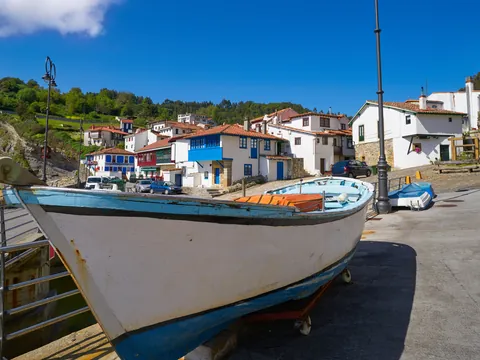 Barca pesquera en el puerto de Tazones con casas al fondo