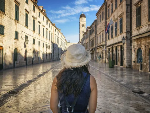 Mujer con sombrero paseando por la calle Stradun de Dubrovnik, al fondo la torre del reloj del casco antiguo.