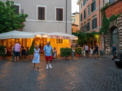 Plaza animada de Trastevere en Roma con una trattoria y gente paseando al atardecer