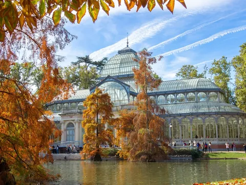 Palacio de Cristal rodeado de árboles y estanque en El Retiro, Madrid.