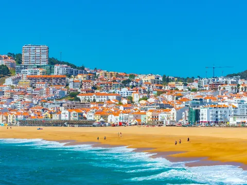 Vista de la playa de Nazaré con casas de tejados rojos y mar azul en un día soleado.