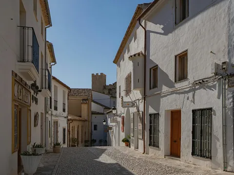 Calle empedrada con casas blancas en Guadalest, con la torre del castillo al fondo.
