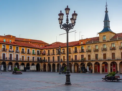 Plaza Mayor de León al atardecer, con edificios porticados, balcones y farolas de hierro, en el centro histórico.