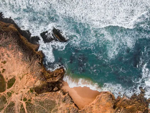 Vista aérea de la playa de Guincho con acantilados y olas rompiendo en la costa.
