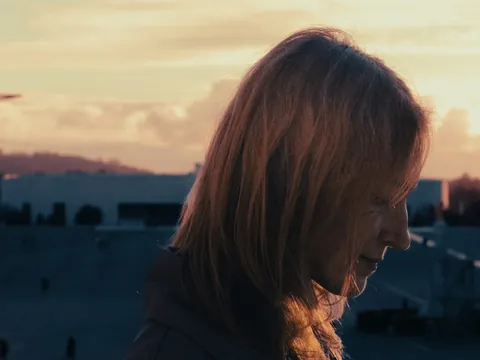 Mujer con cabello rojizo al atardecer en el Santuario de Fátima, silueta de la cruz y la Basílica de la Santísima Trinidad.