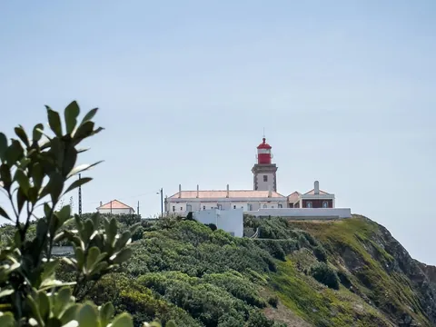 Faro de Cabo da Roca sobre un acantilado rodeado de vegetación y cielo claro.