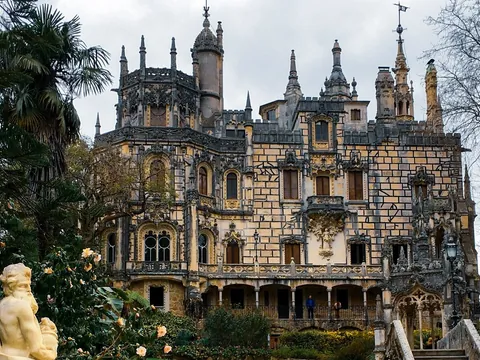 Fachada del Palacio da Regaleira en Sintra vista entre jardines y esculturas.