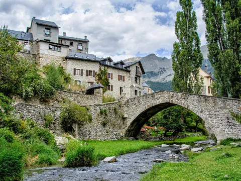 Puente de piedra sobre el río en Sallent de Gállego, con casas tradicionales pirenaicas y montaña de fondo, Huesca.