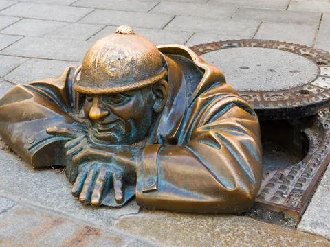 Escultura de Čumil en Bratislava, un hombre de bronce asomando desde una alcantarilla en la acera.