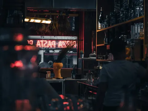 Interior tenue de un bar en Berlín con letrero de neón rojo de pizza y pasta.