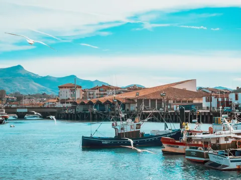 Barcos pesqueros en el puerto de San Juan de Luz con montañas al fondo.