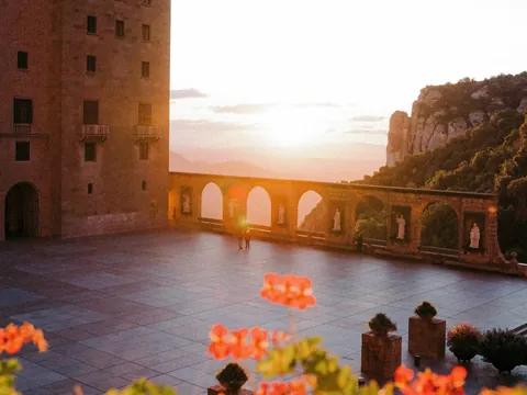 Patio del monasterio de Montserrat al atardecer, con arcos y montañas al fondo.