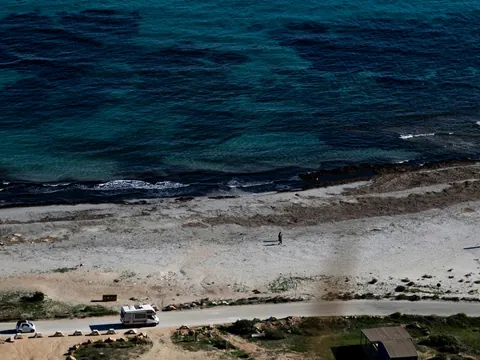 Vista aérea de una playa de arena y rocas con caravanas y una persona, junto al mar turquesa de Santa Pola.