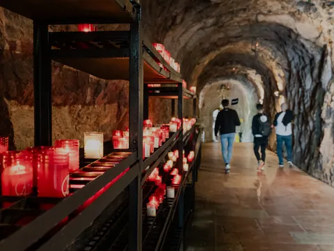 Interior del Santuario de Covadonga, con velas encendidas junto a la cueva y visitantes recorriendo este lugar sagrado.
