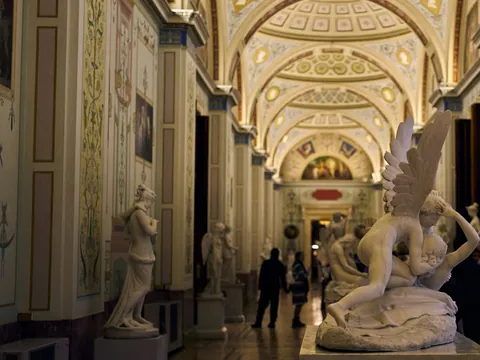 Interior de la Galería Uffizi en Florencia, con un pasillo ornamentado y esculturas clásicas de mármol, destacando en primer plano la obra 'Psique reanimada por el beso de Cupido.